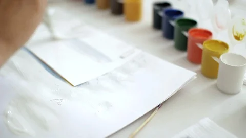 Close-up hand holds a brush, drawing with white paints on a sheet of paper. Stock Footage 115925544