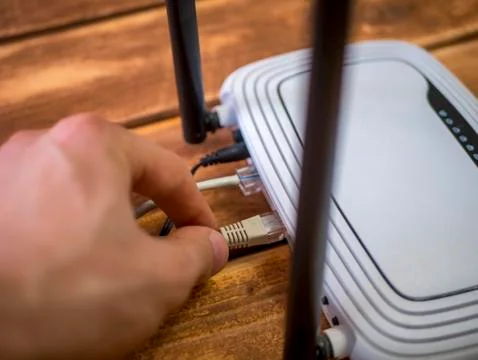 Close up hand inserting ethernet wire in wi-fi router on wooden table Stock Photos