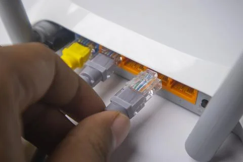 Close-up of a hand inserting a grey Ethernet cable into a LAN port on a whi.. Stock Photos