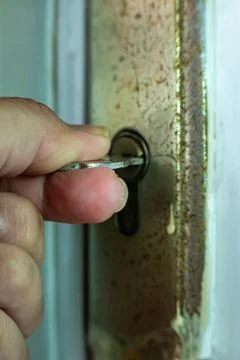 Close-up of a hand inserting a key into an old rusty door Stock Photos