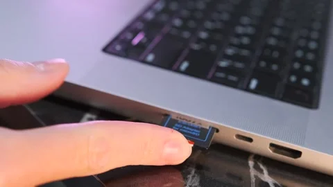 Close-up of hand inserting SD memory card into laptop slot for data storage Stock Footage 333650366
