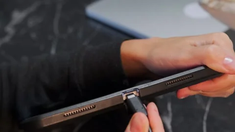 Close-up of hand inserting USB-C cable into tablet port for charging and data Stock Footage 333649472