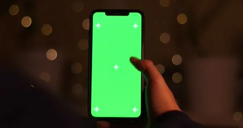 Close-up of a hand interacting with a green screen smartphone in bokeh lighting Stock Footage 339071939