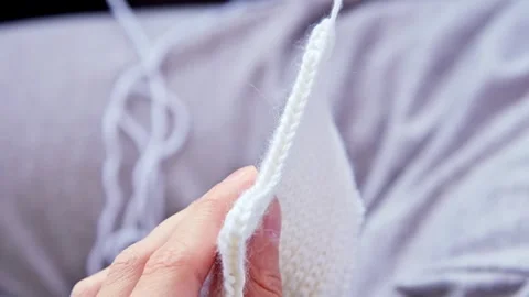 Close-up of a hand knitting a white fabric piece, showing the progression of Stock Footage 330939866