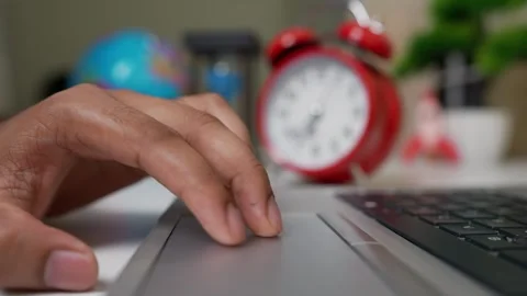 Close-up of a hand on a laptop touchpad with a blurred clock and globe in t.. Stock Footage 316745229