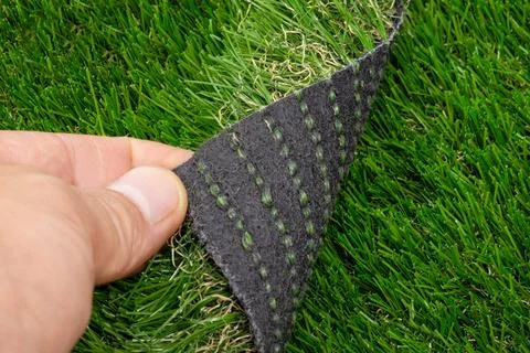 Close-up of a hand lifting artificial grass to expose the black backing with Foto stock