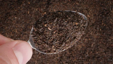 The close-up of a hand lifting a spoon with dried black tea leaves upwards, with Video stock 265771780