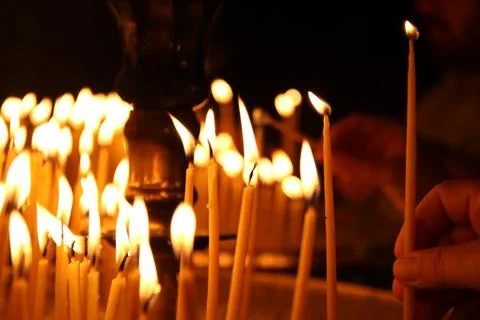 Close-up of a hand lighting a candle during a warm, candlelit ritual in Greec Stock Photos