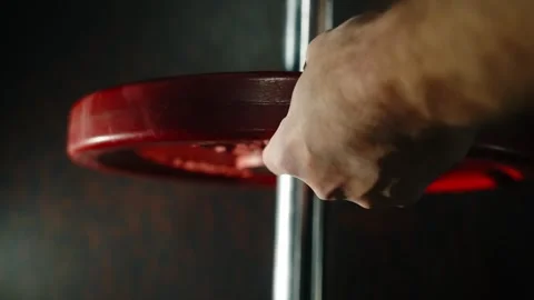 Close-up of a hand loading a red weight plate onto a barbell in the gym 库存影片 329557457
