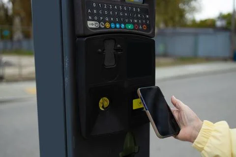 Close up of hand making contactless smartphone payment at city parking meter. Stock Photos
