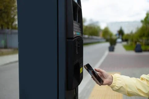 Close up of hand making contactless smartphone payment at city parking meter. Stock Photos