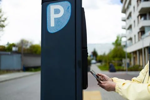 Close up of hand making contactless smartphone payment at city parking meter. Stock Photos