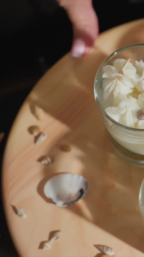 Close up of hand moving around seashell decorated cream wax candles on wooden Stock Footage 347625037