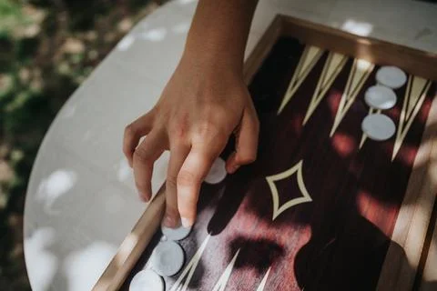 Close-up of a hand moving pieces on a backgammon board, captured in natural Stock Photos