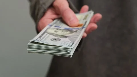 Close-up of a hand offering a thick stack of hundred-dollar bills, symbolizing Stock Footage 304031538
