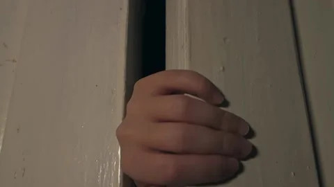 A close-up hand opening the door, from behind which a teenage girl peeps. Stock Footage 144287994