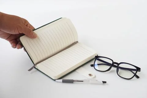 Close-up of hand opening a lined notebook with pen and eyeglasses on white backg Stock Photos