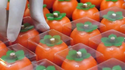 Close-up of Hand Packing Persimmon-Shaped Traditional Desserts into Clear Boxes Stock Footage 345292206