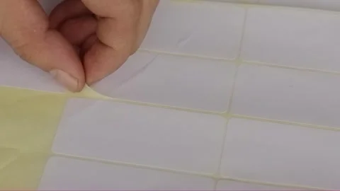 Close-up hand peeling blank white adhesive label from sheet Video stock 320129059