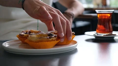 Close-Up of a Hand Picking a Dessert from a Plate Next to Tea on a Café Table Stock Footage 304287514