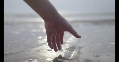 Close-up of a hand picking up a discarded plastic bottle from the shoreline Stock-Footage 340364439