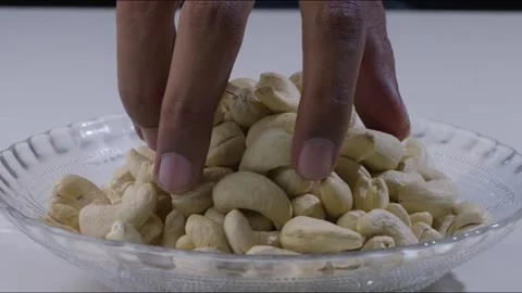 Close up of hand picking up handful of cashew nuts from plate on table. Static Stock Footage 280261756