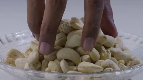Close-up of hand picking up a handful of cashew nuts from the plate on the table Stock Footage 287849827