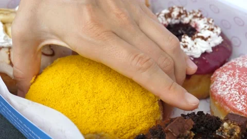Close up of a hand picking up one of the vegan donuts from the box. Selection of Video stock 158383362