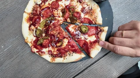 Close-Up of Hand Picking Up Pepperoni Jalapeño Pizza Slice on Rustic Table Stock Footage 340538672