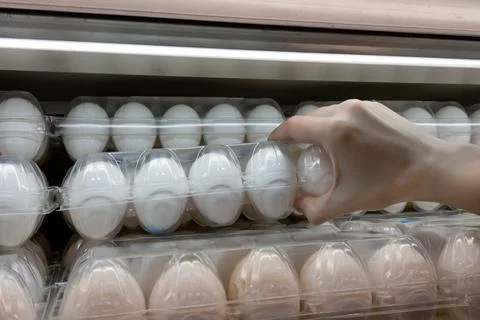 Close-up hand picking raw of eggs in a plastic egg tray from shelf in store. Stock Photos