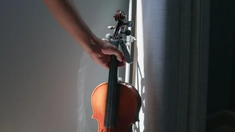 Close up hand picking up a violin with sun light and curtains background Stock Footage 306005747