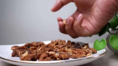 Close-up of a hand picking walnuts from a plate with a plant in the backgroun Stock Footage 318057166