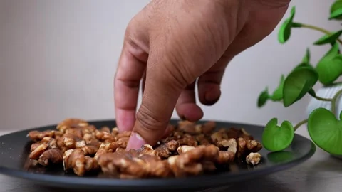 Close-up of a hand picking walnuts from a plate with a plant in the backgroun Stock Footage 318057169