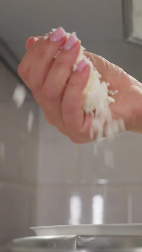 Close up of hand with pink nails squeezing cooked rice over white bowl in soft Stock Footage 344674147