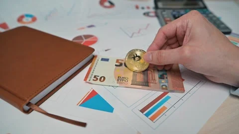 A close-up of a hand placing a Bitcoin coin on euro banknotes. Comparison, Stock Footage 338301522