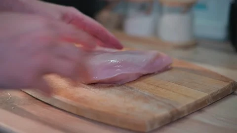 Close-up of a hand placing a chicken breast fillet on a wooden board 库存影片 338301313