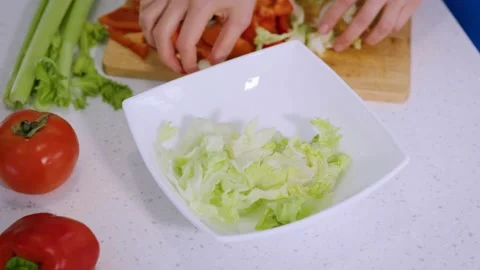Close-up of a hand placing chopped vegetables in a white salad plate Stock Footage 234870438