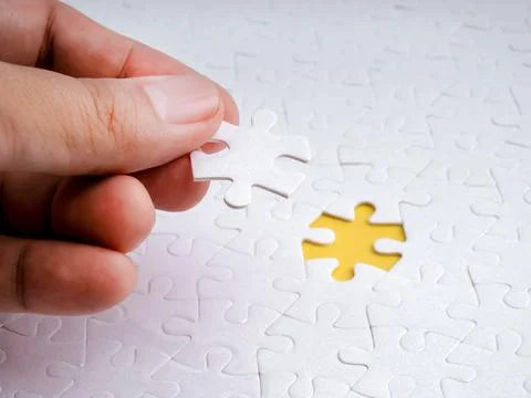 Close-up hand placing final puzzle piece into missing spot on white jigsaw,.. 库存照片