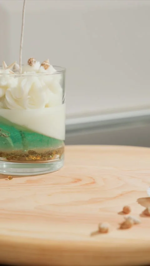 Close up of hand placing lit wick into layered sea themed candles on wooden Stock Footage 345732933