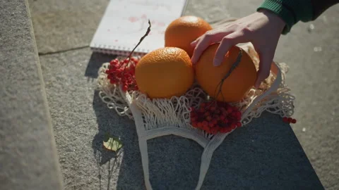 Close up of hand placing orange into net bag surrounded by red berries on Stock Footage 347702753