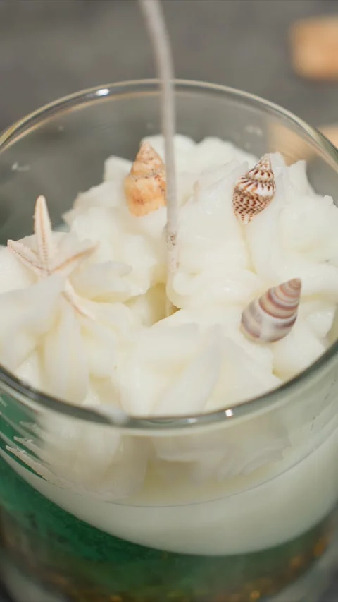 Close up of hand placing seashell and starfish decorations into white wax for Vídeo Stock 344674185