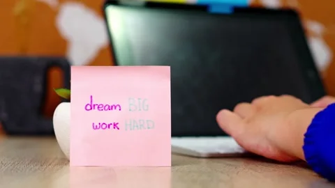 Close-up of Hand placing sticky note with "dream BIG work HARD" on desk front Stock Footage 330888964