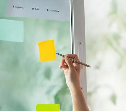 Close-up of hand placing sticky note on window for task management 库存照片