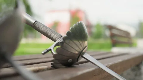 Close up hand placing two fencing swords on wooden bench in park with soft Stock Footage 345835156