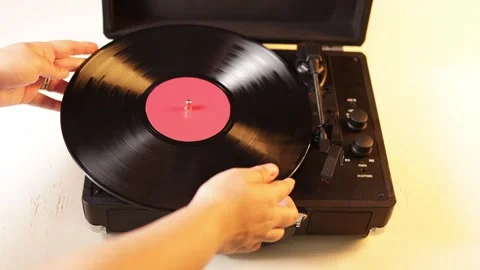 Close-up of a hand placing a vinyl record onto a portable turntable Stock Footage 339004577