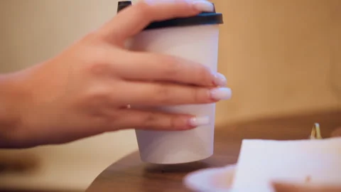 Close up hand placing white travel mug with black lid on wooden table in warm Stock Footage 346729708
