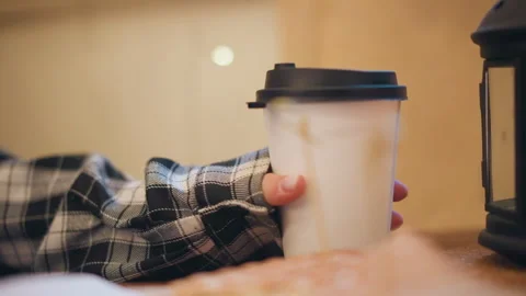 Close up of hand in plaid sleeve reaching steady grip on disposable coffee cup Stock Footage 346729406