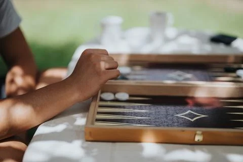 Close-up of a hand playing a backgammon game outdoors on a sunny day, evoking Stock Photos