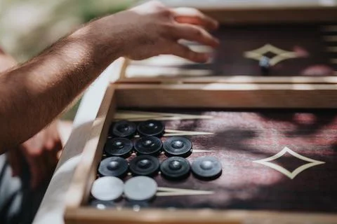 Close-up of a hand playing backgammon outdoors on a sunny day, highlighting Stock Photos