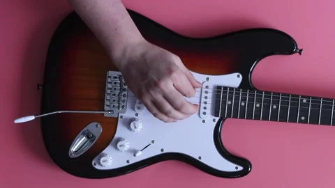 Close-up of a hand playing an electric guitar with a sunburst finish on a pink Stockbeeldmateriaal 339190915